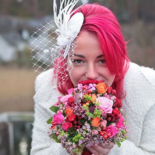 Hochzeitsfloristik Frau mit pinken Haaren in Hochzeitskleidung hält einen bunten Blumenstrauß vor sich.